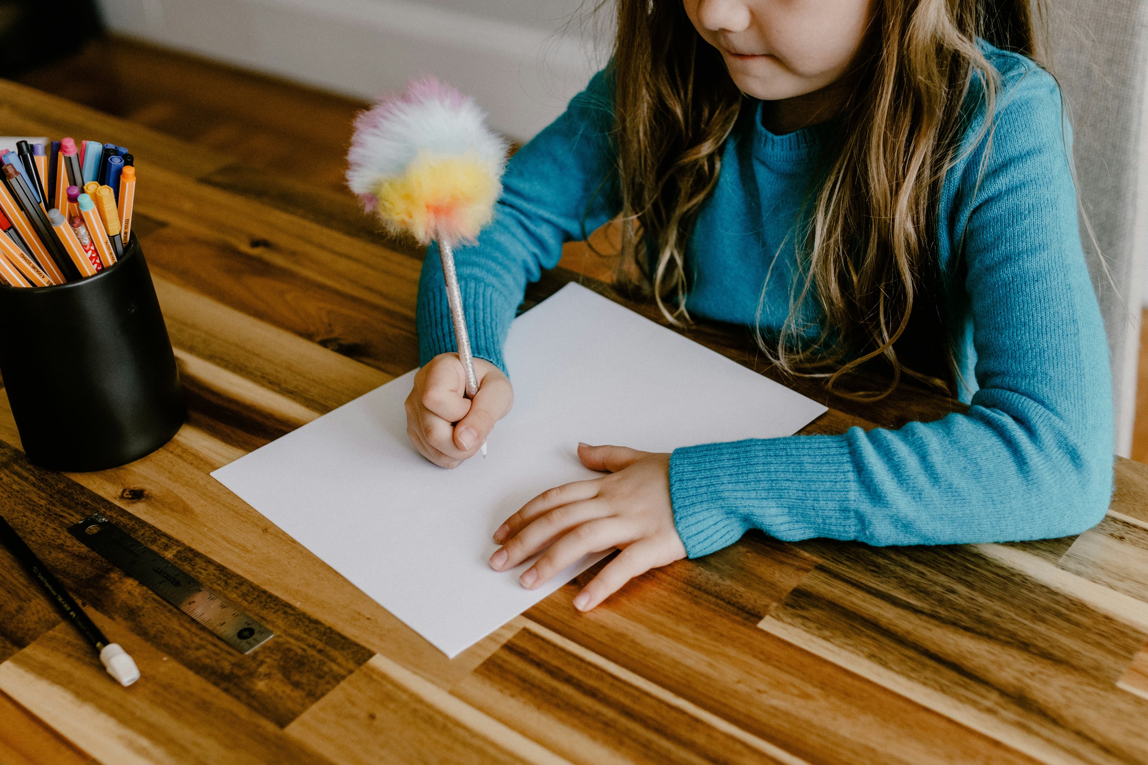 A child handwriting at a desk surrounded by colorful pens and markers