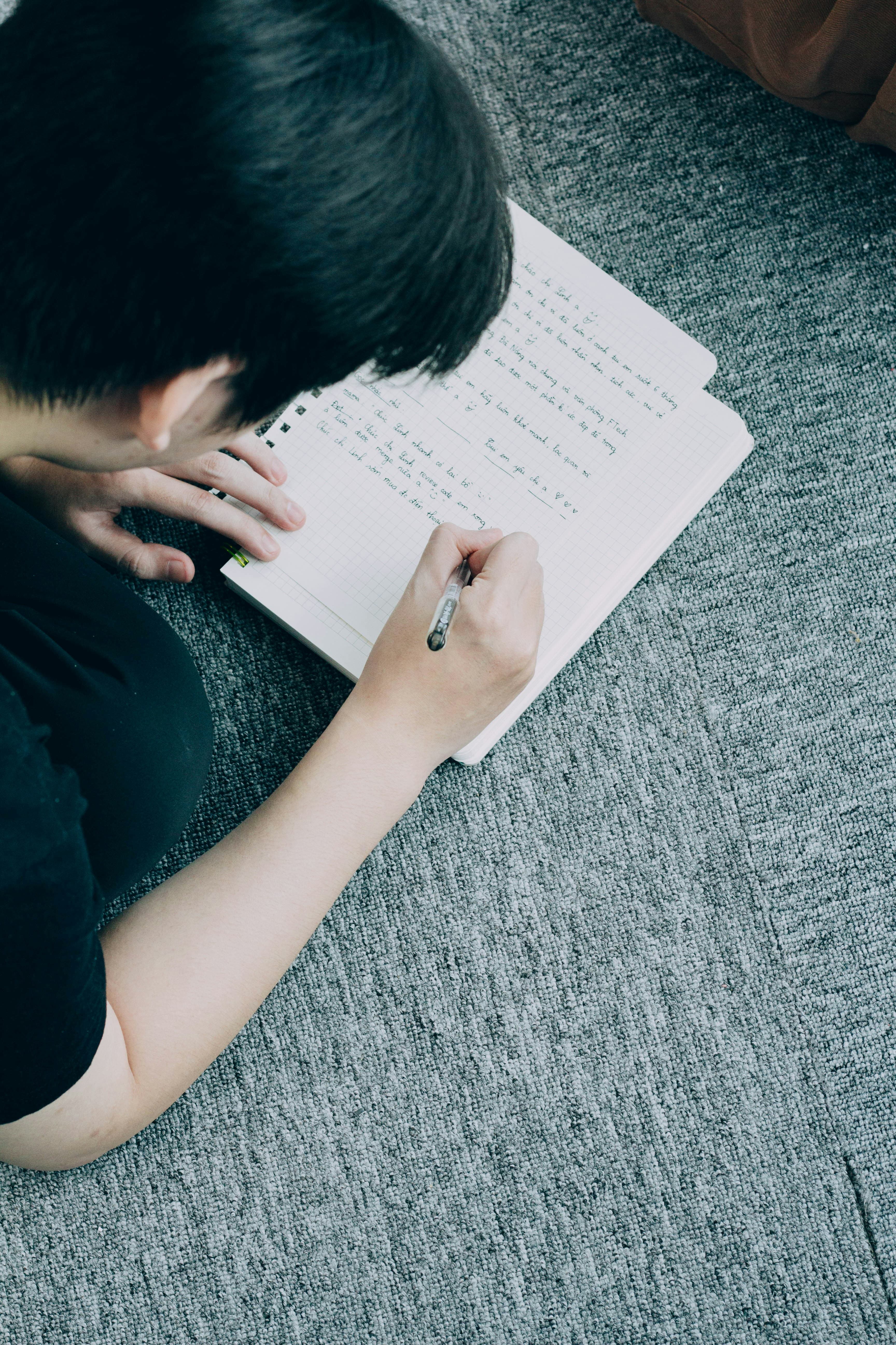 A child handwriting in a notebook on the floor